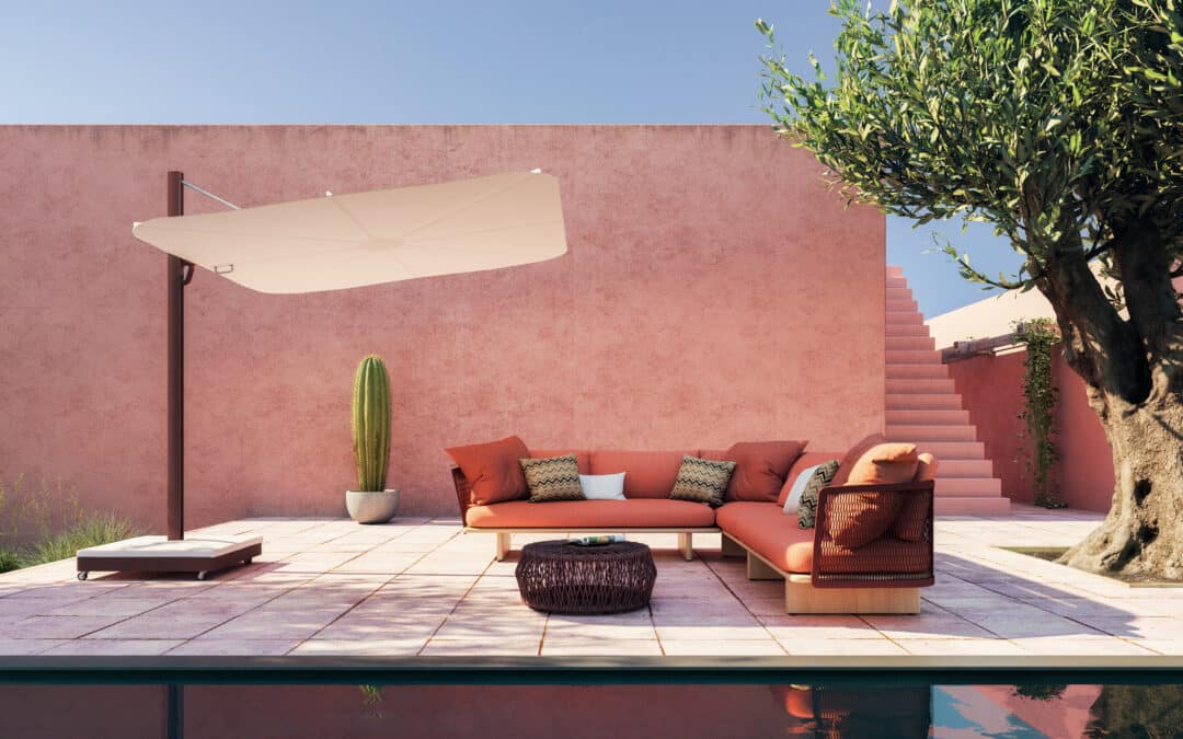 Patio en ton rose avec canapé d’angle terracotta, table tressée et grand parasol au bord d'une piscine